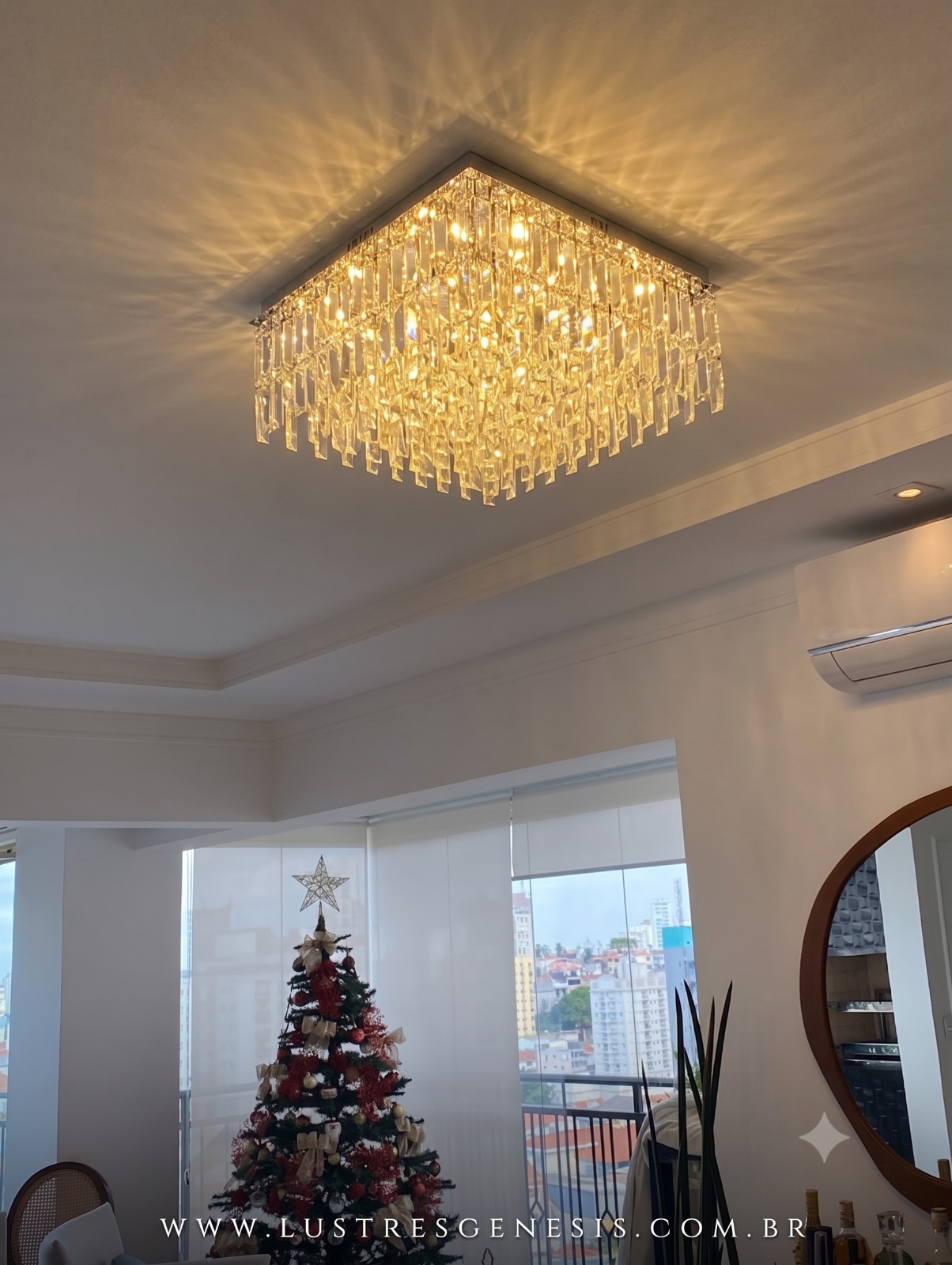 Lustre plafon de cristal quadrado Kalista 50x50cm instalado no teto de uma sala de estar decorada, com árvore de Natal ao fundo e iluminação elegante.